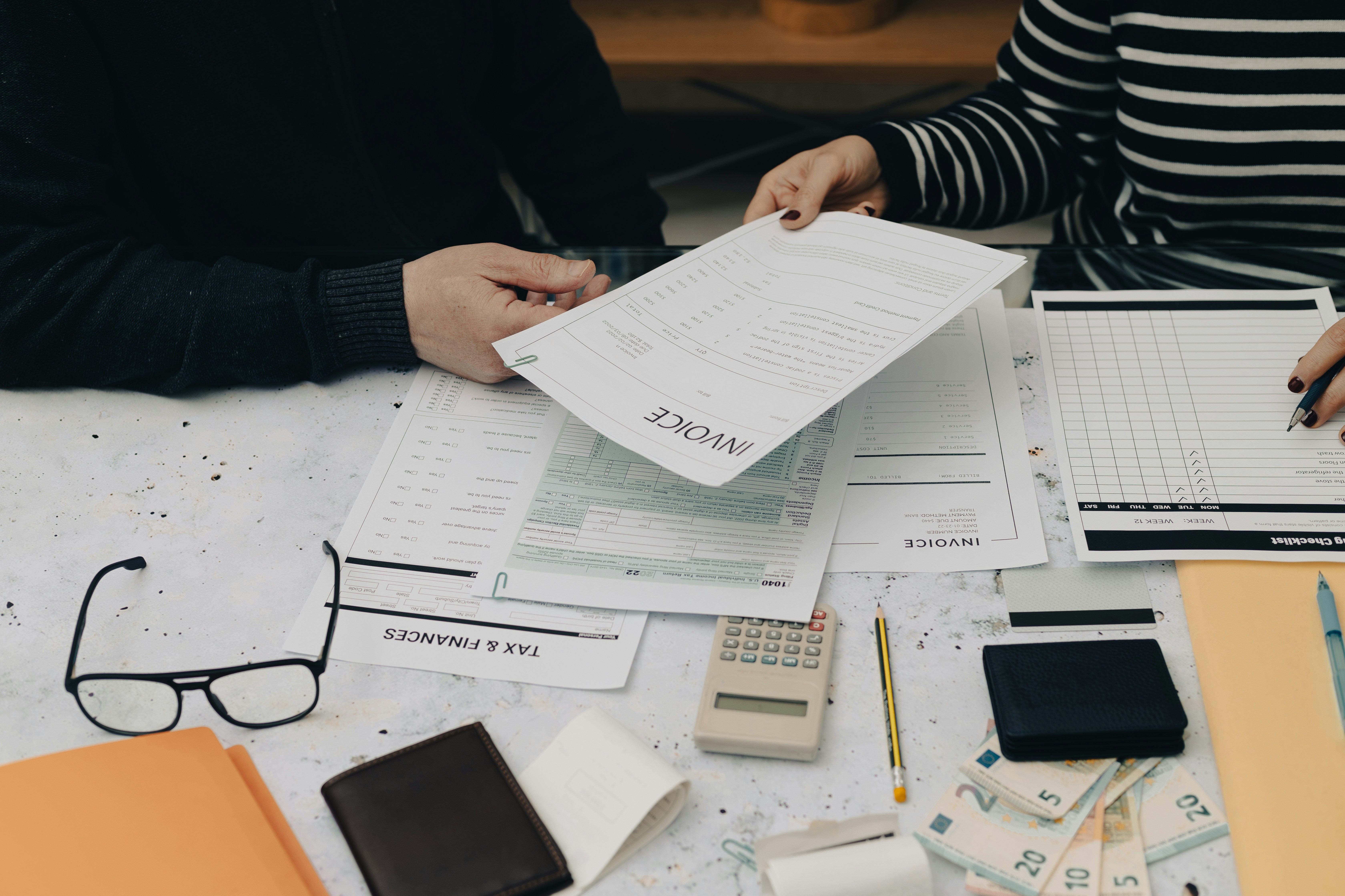 Two people at a desk reviewing invoices and financial documents using a checklist