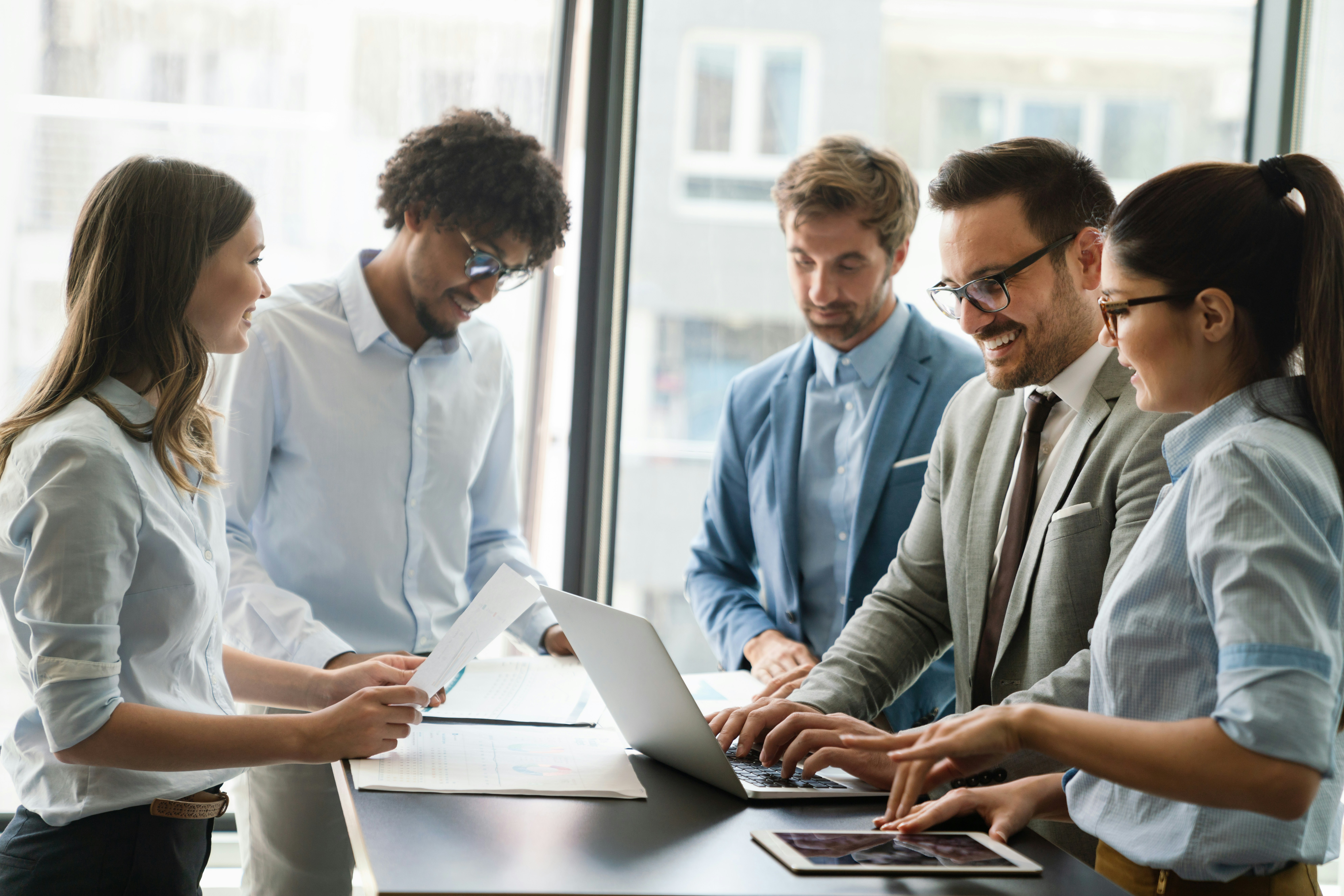 Team gathered around a table, reviewing documents and viewing information on a laptop