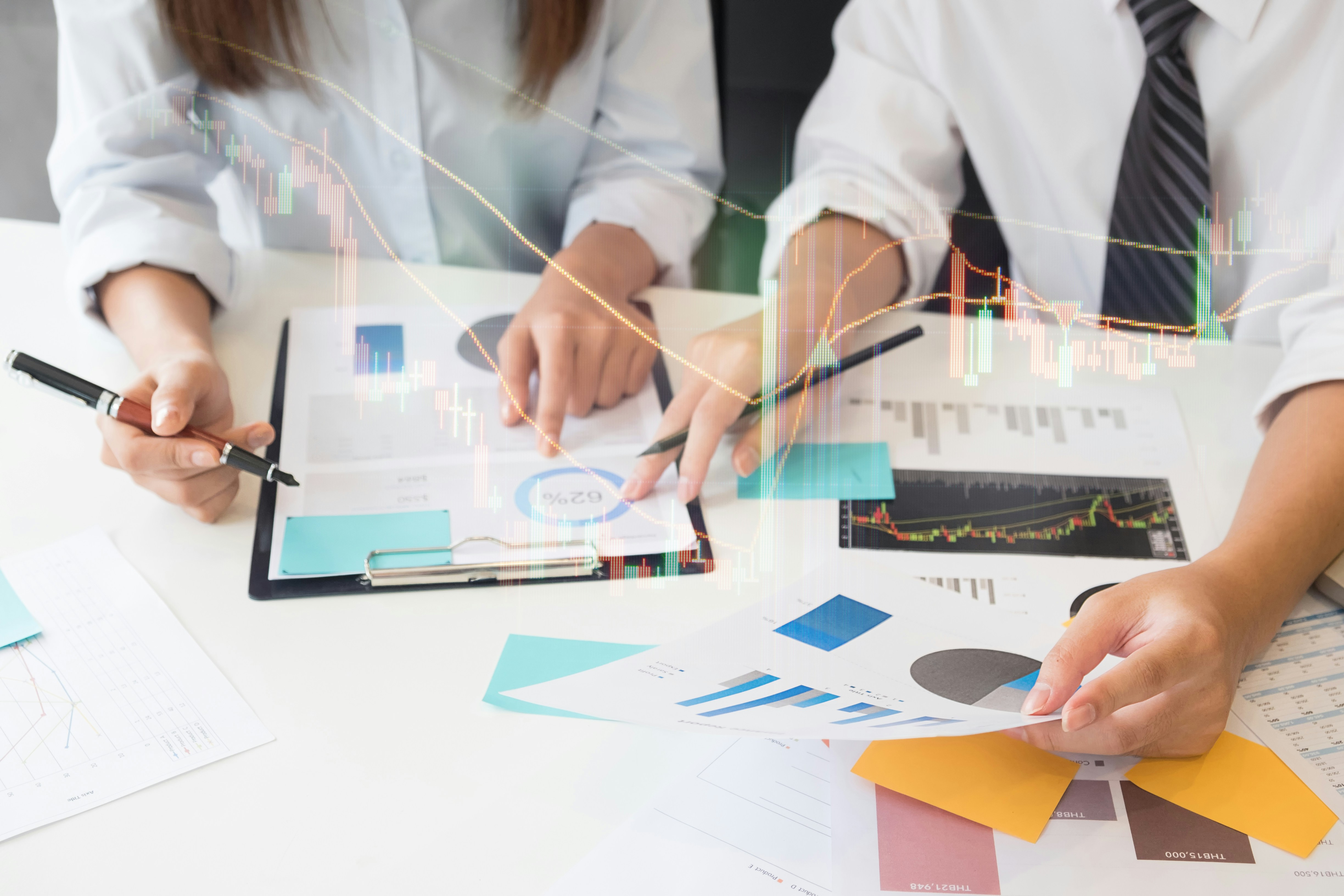 Two people reviewing financial charts and reports on a desk.