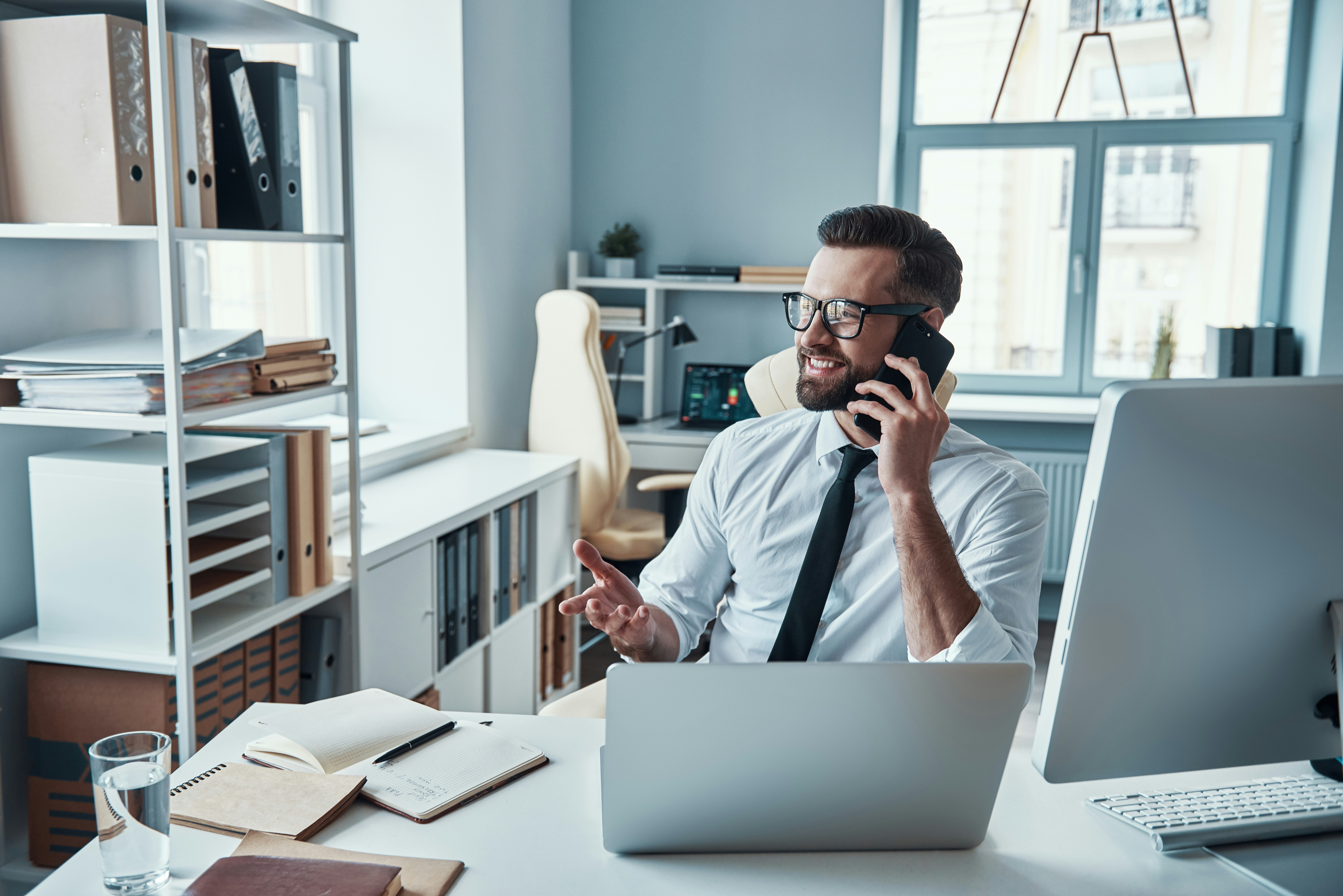 Financial advisor speaking on the phone at a desk with a laptop and documents.